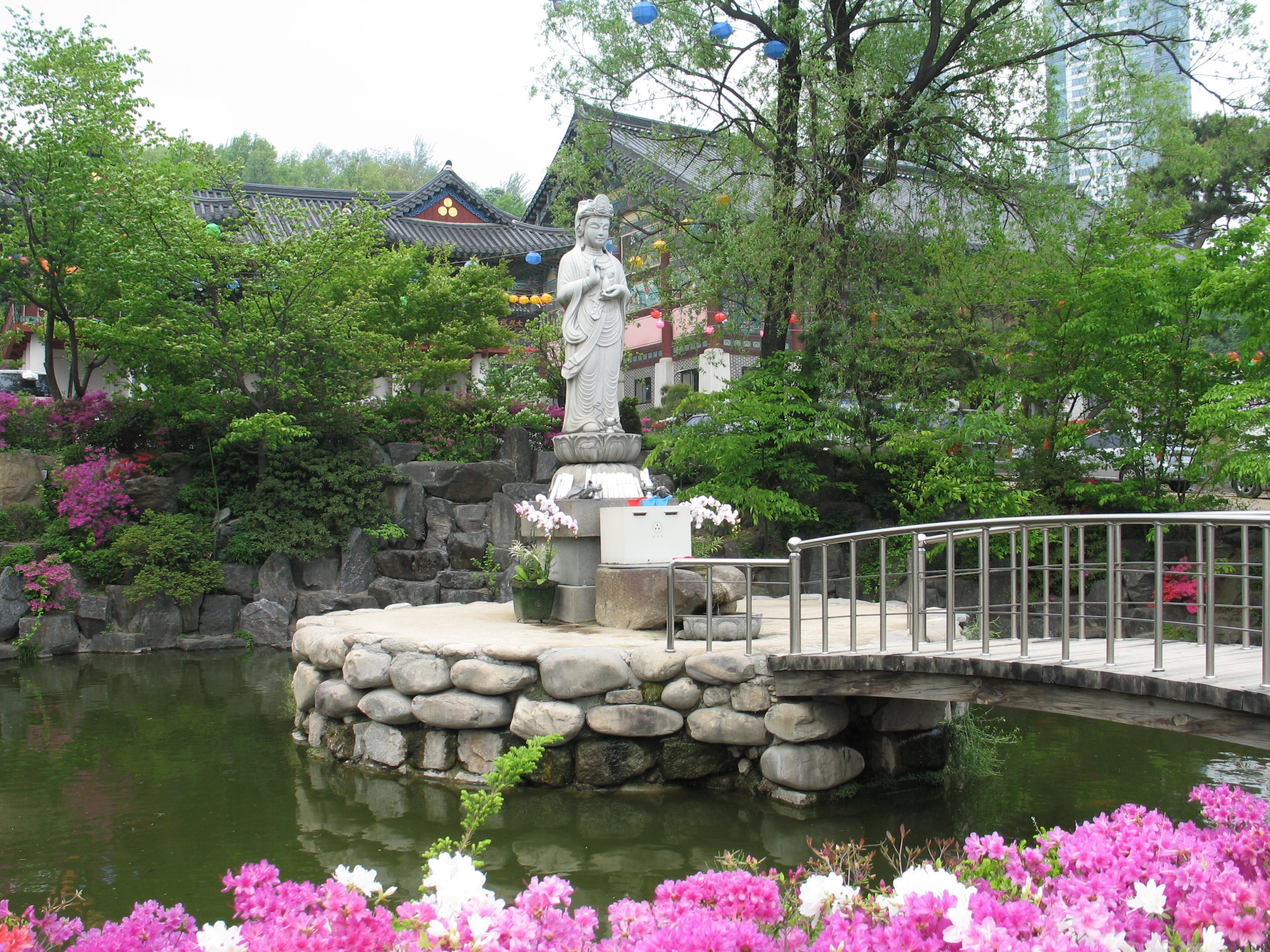 Stone Bodhisattva statue in a garden pond with spring azaleas at Bongeunsa Temple