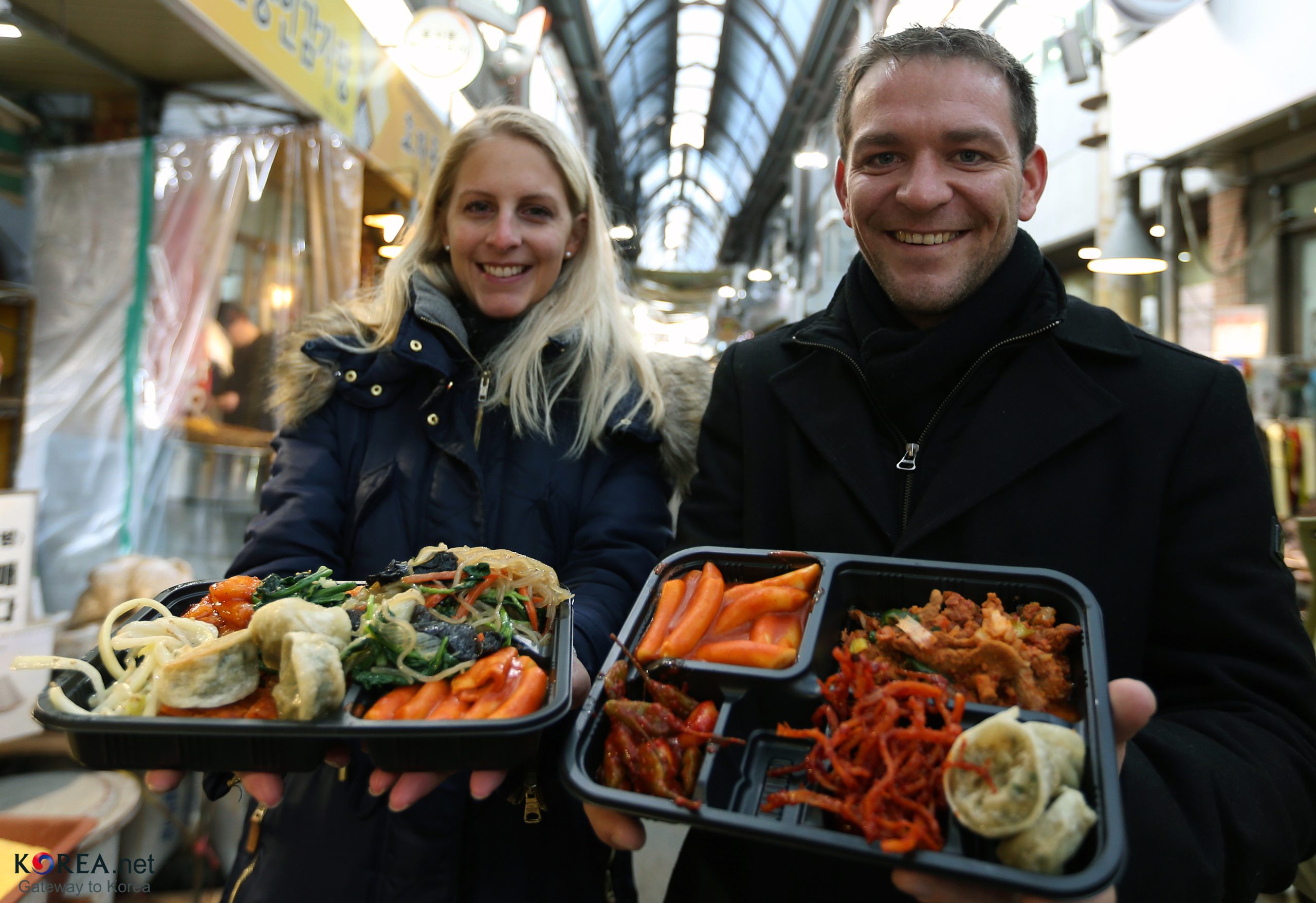 Visitors holding filled brass-coin dosirak lunchbox trays at Tongin Market