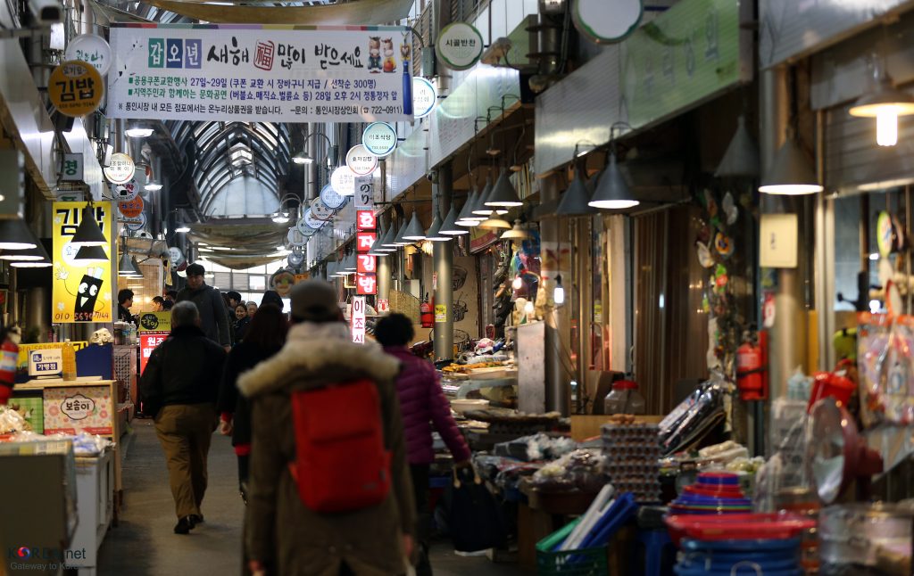 A busy aisle inside Tongin Market with stalls and the lunchbox-cafe banner