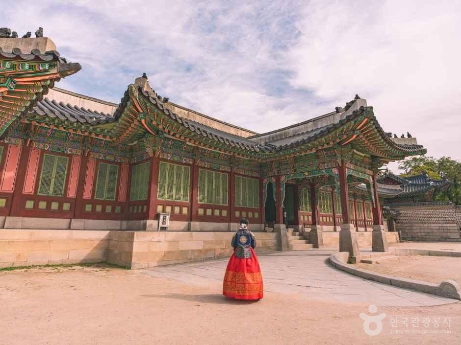 Visitor in red hanbok before a painted hall at Changdeokgung Palace, Seoul