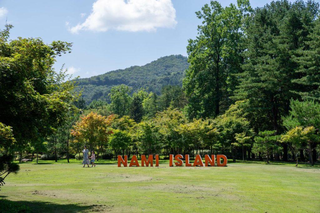 Nami Island entrance lawn with the island name sign and forested hills behind